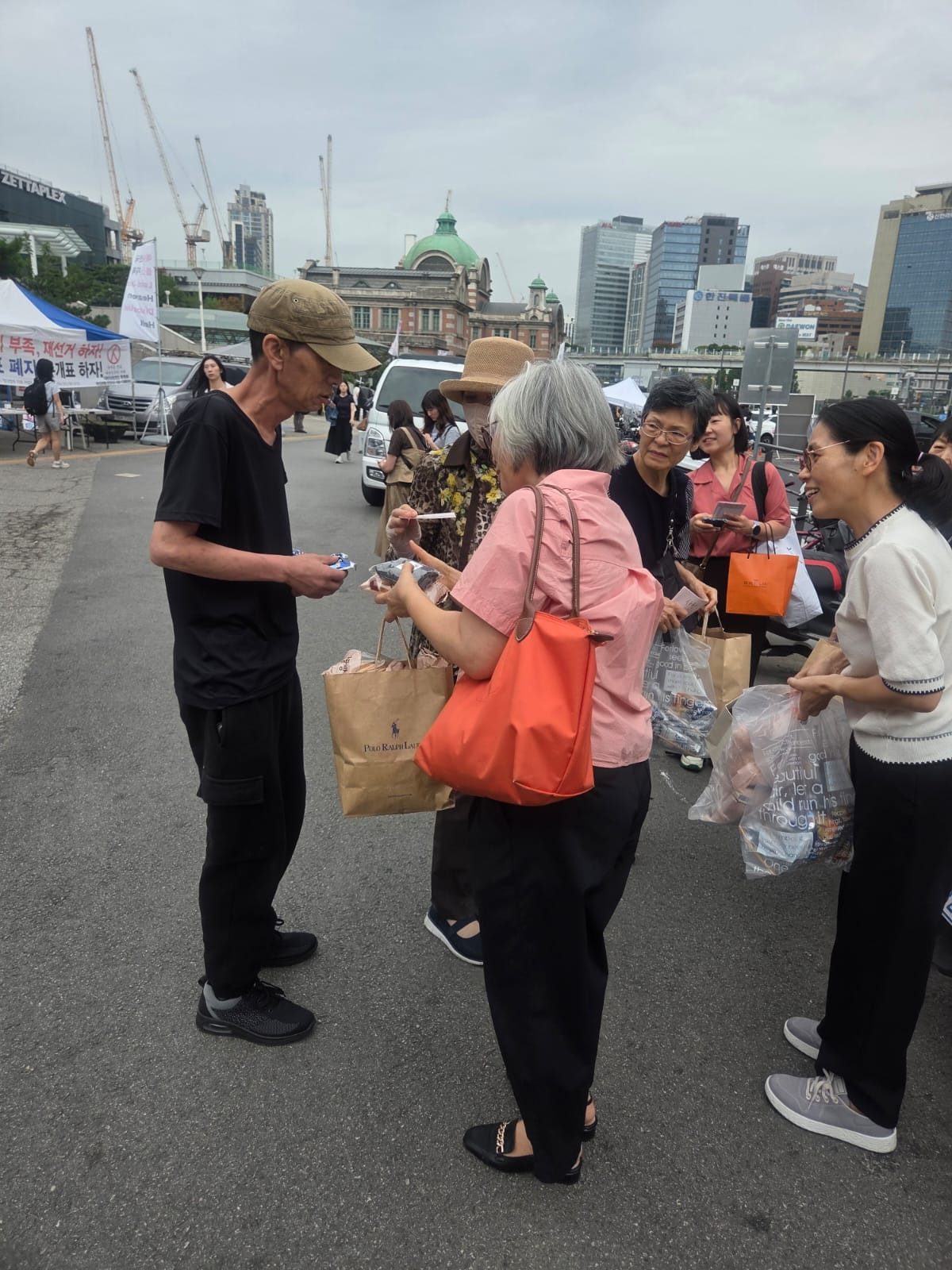 야외에서 여러 성인이 포장물과 종이봉투를 들고 마주 서 있는 모습