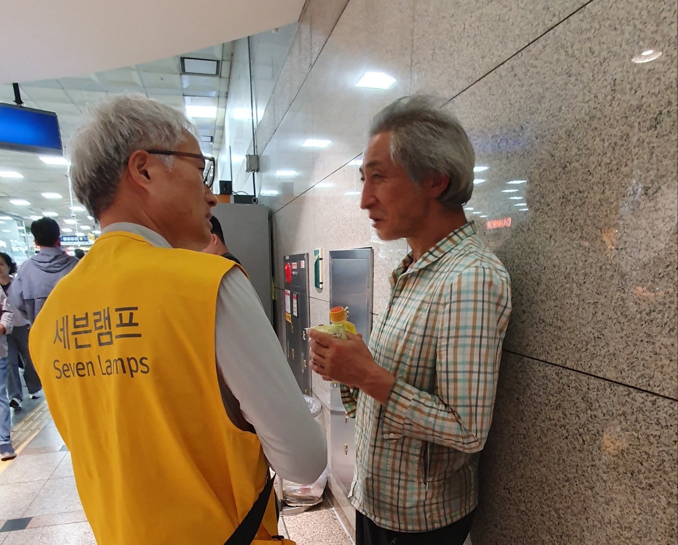 실내 통로에서 음료를 들고 이야기를 나누는 모습
