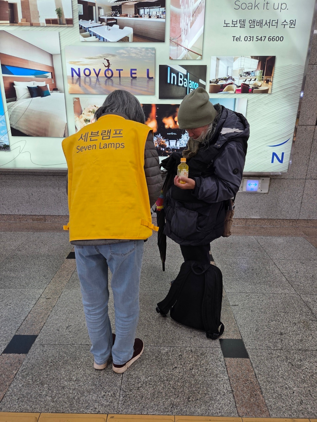 역 안 광고판 앞에서 물품을 건네는 모습